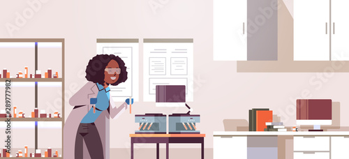 scientist holding test tubes with blood samples african american woman in uniform using analyzer medical machine research science medicine concept modern laboratory interior portrait horizontal