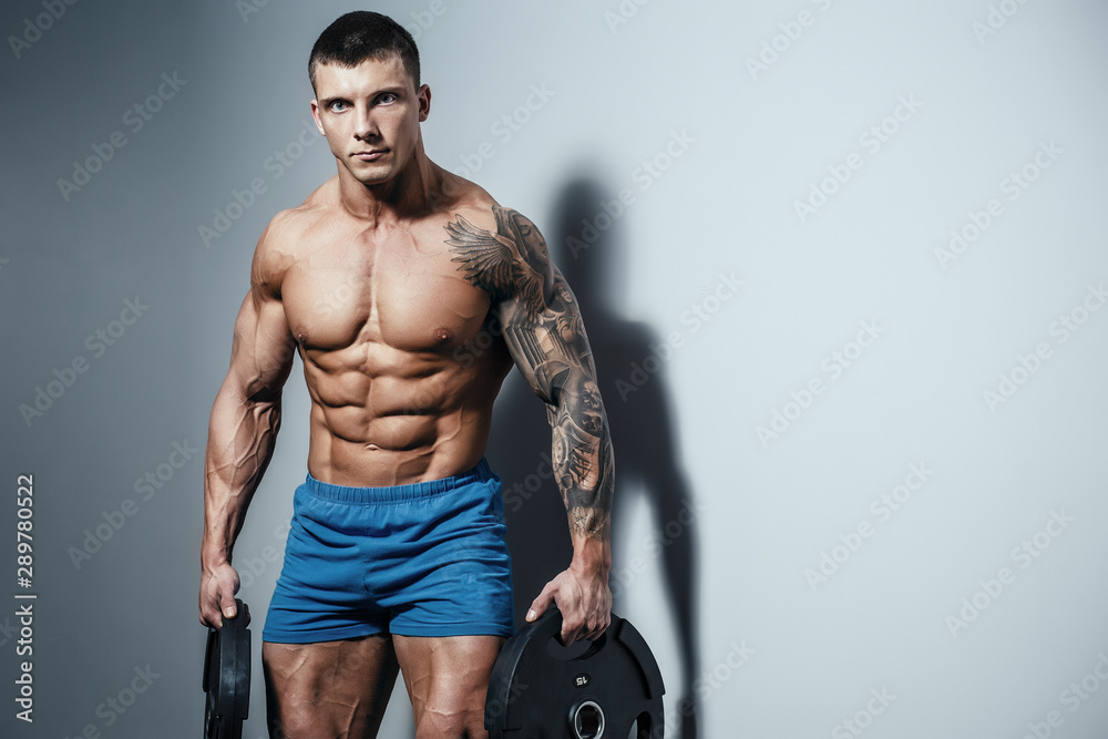 Muscular man bodybuilder training in gym and posing. Fit muscle guy workout with weights and barbell Muscular man bodybuilder training in gym and posing. Fit muscle guy workout with weights and barbell
