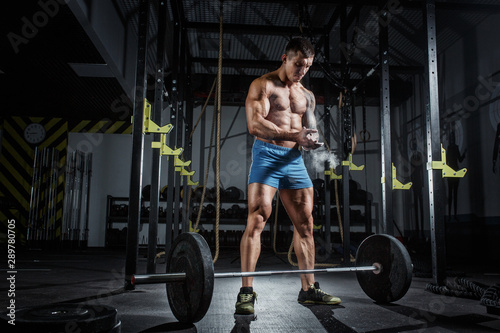 Athletic pumped man bodybuilder stands in front of bar in gym