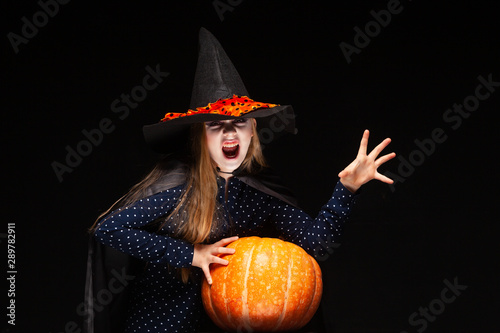 Halloween Witch with Pumpkin on black background Casts a spell with his hands. Beautiful young surprised woman in witches hat and costume holding pumpkin. Wide Halloween party art design. Copy-paste