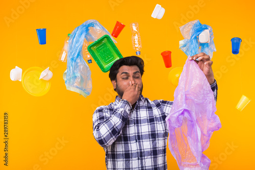 Environmental pollution, plastic recycling problem and ecology problem concept - surprised Indian man closing nose because he is felt bad smell from garbage on yellow background. photo