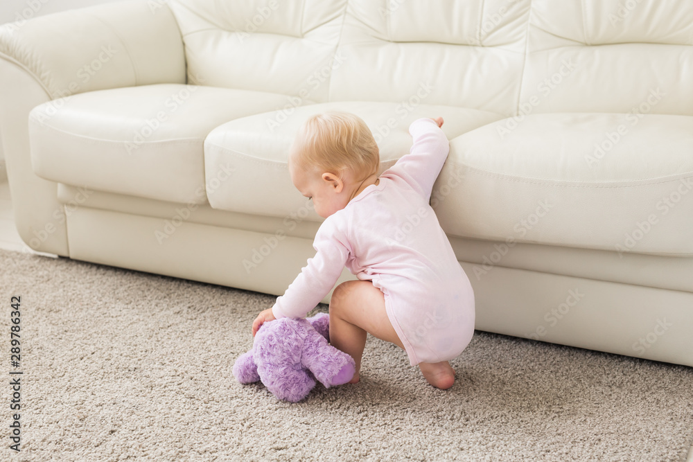 childhood, babyhood and people concept - happy little baby girl playing near couch at home childhood, babyhood and people concept - happy little baby girl playing near couch at home