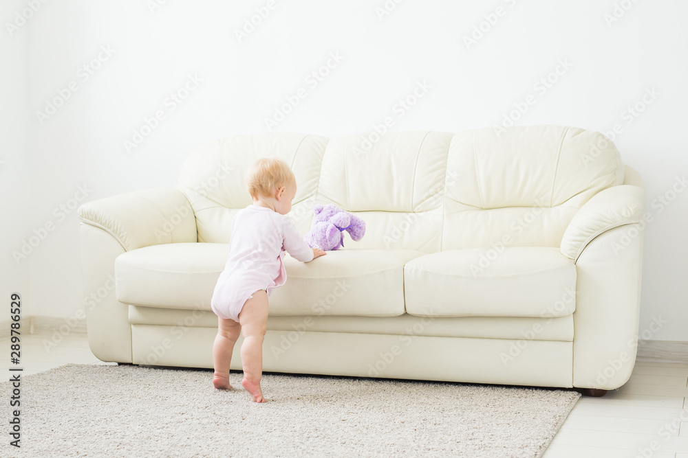 childhood, babyhood and people concept - happy little baby girl playing near couch at home childhood, babyhood and people concept - happy little baby girl playing near couch at home
