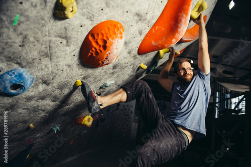 happy smiling young active caucasian bearded male in glasses during workout in climbing indoor gym hanging fun