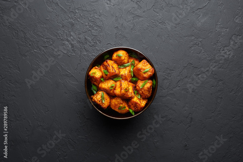 Paneer Manchurian or Paneer 65 in bowl at black concrete background. Paneer Manchurian is Indian Chinese cuisine dish with panner cheese, tomatoes, onion, soy sauce. Copy space
