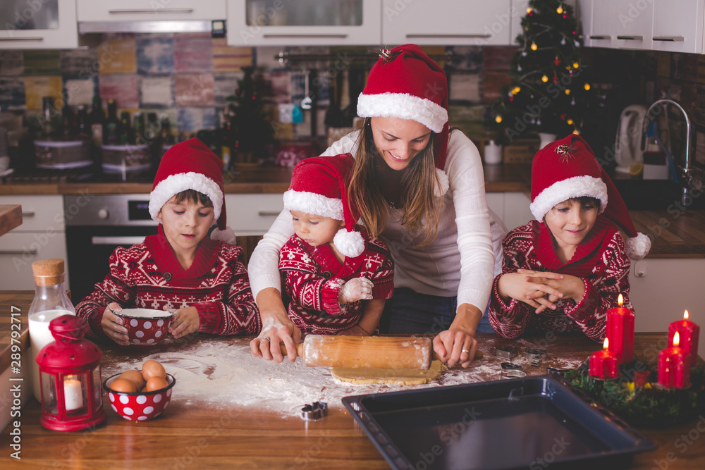 Sweet toddler child and his older brother, boys, helping mommy preparing Christmas cookies at home .