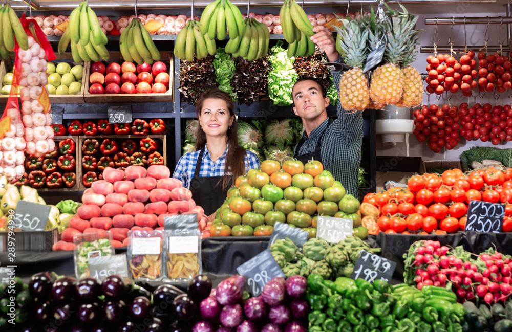 Friendly man and woman laying out vegetables and fruits in shop
