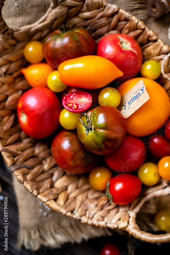 overhead shot of homegrown assorted red  yellow  orange tomatoes in wicker straw basket on sackcloth on rustic wooden table  autumn harvesting 