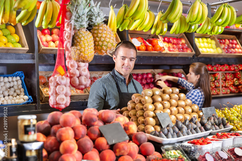 Man selling fresh kiwi and other fruits on supermarket
