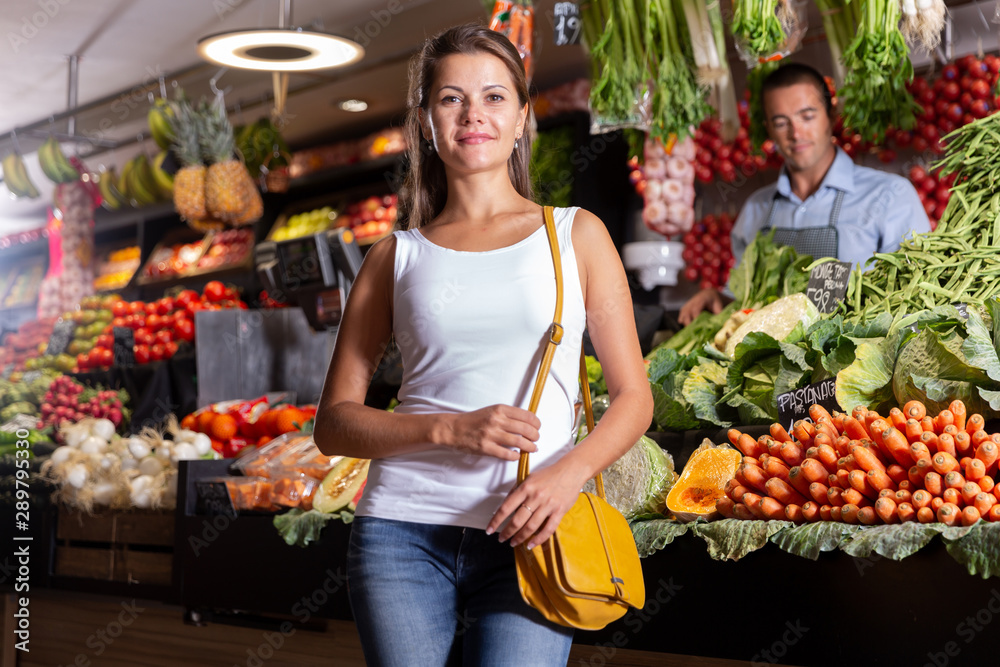 Cheerful female customer standing near counter with fresh fruits