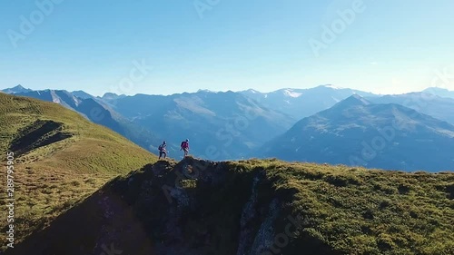 Zoomed in aerial drone shot of a couple walking along an Alpine mountain ridge with a stunning mountain landscape in the background. Hikers on a summer adventure in the Austrian Alps. photo