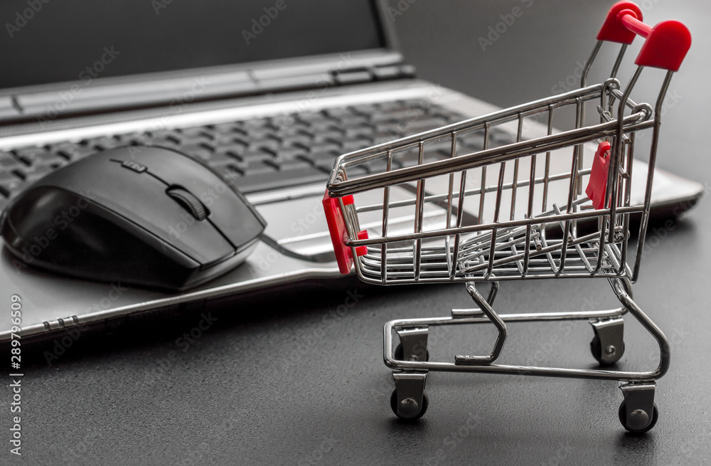 Shopping cart with laptop on black background. Online shopping concept.