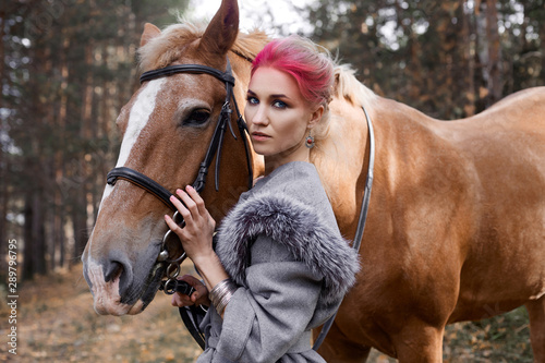 Woman on a horse in the fall. Creative bright pink makeup on the girl face, hair coloring. Portrait of a girl with a horse. Horseback riding in the autumn forest. Autumn clothes