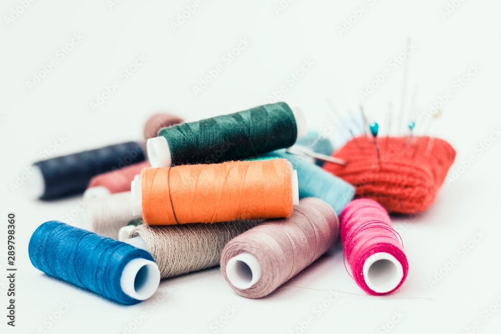 Tools for needlework, red knitted needle pad for sewing and colored thread coils on white background with copy space for text. Tools for needlework, red knitted needle pad for sewing and colored thread coils on white background with copy space for text.