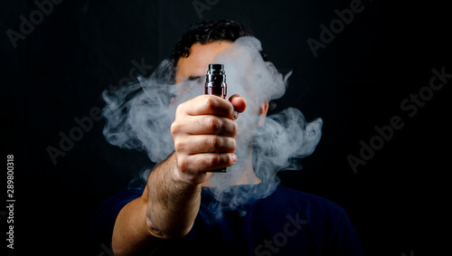 hand holding vape e-cigarette or electronic cigarette with white smoke over a black background. 