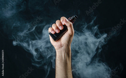 hand holding vape e-cigarette or electronic cigarette with white smoke over a black background.  photo