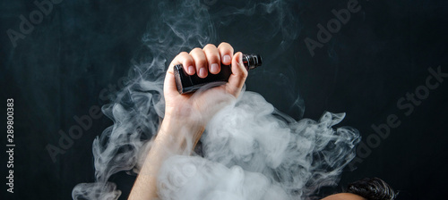 hand holding vape e-cigarette or electronic cigarette with white smoke over a black background. 