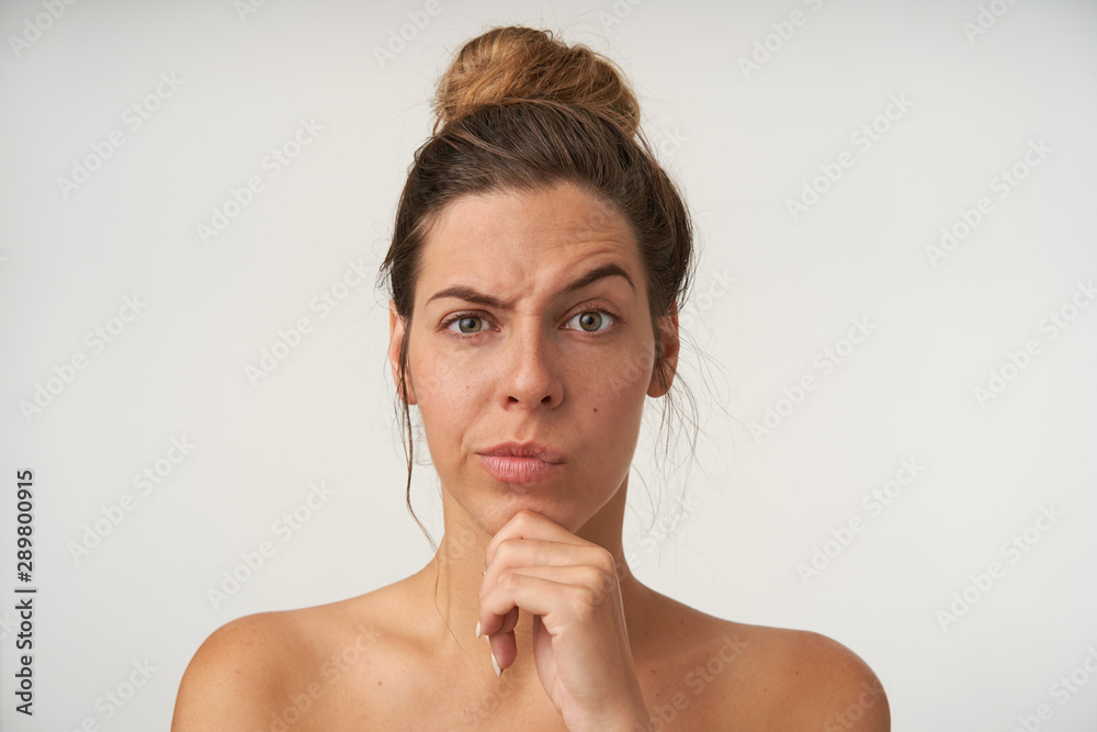 Young beautiful pensive female posing over white background with casual hairstyle, frowning, raising eyebrow and holding her chin with hand Young beautiful pensive female posing over white background with casual hairstyle, frowning, raising eyebrow and holding her chin with hand
