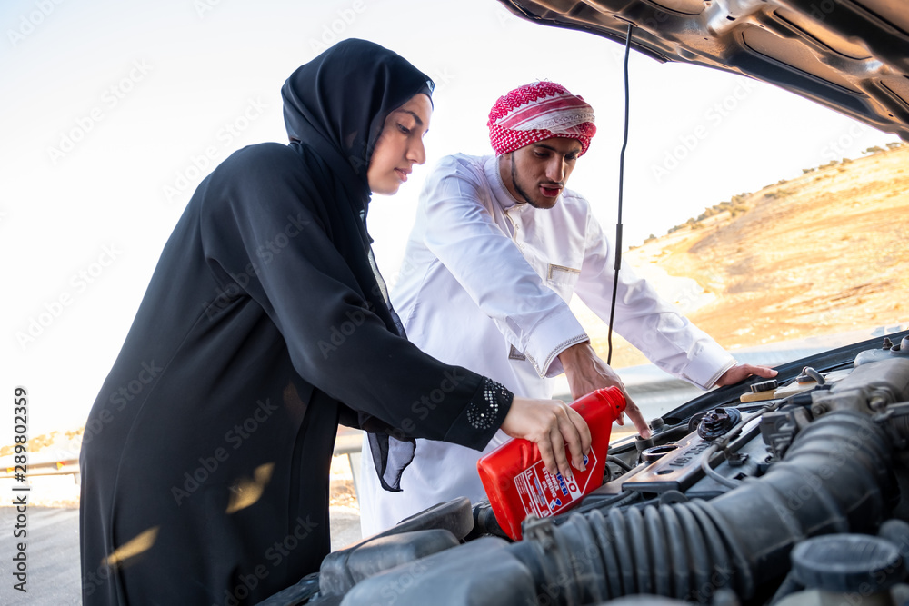Arabic woman and her husband pouring oil in the car engine