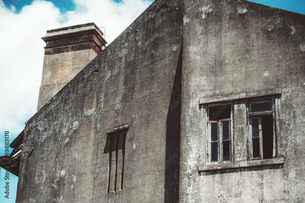 Bottom view of the facade of an abandoned antique building with grey concrete grungy walls, window holes with partly absent glasses inside and the ventiduct on the triangle roof, Sintra, Portugal Bottom view of the facade of an abandoned antique building with grey concrete grungy walls, window holes with partly absent glasses inside and the ventiduct on the triangle roof, Sintra, Portugal
