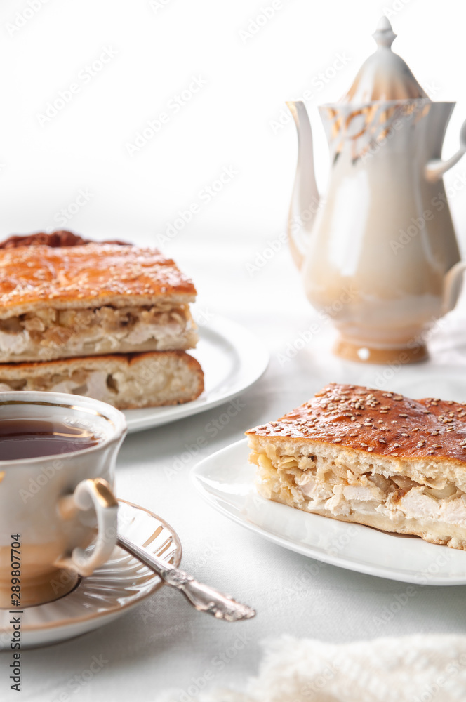 A slice of homemade chicken and sesame pie. On a white plate. Near a coffee pot and a cup of coffee. White background A slice of homemade chicken and sesame pie. On a white plate. Near a coffee pot and a cup of coffee. White background