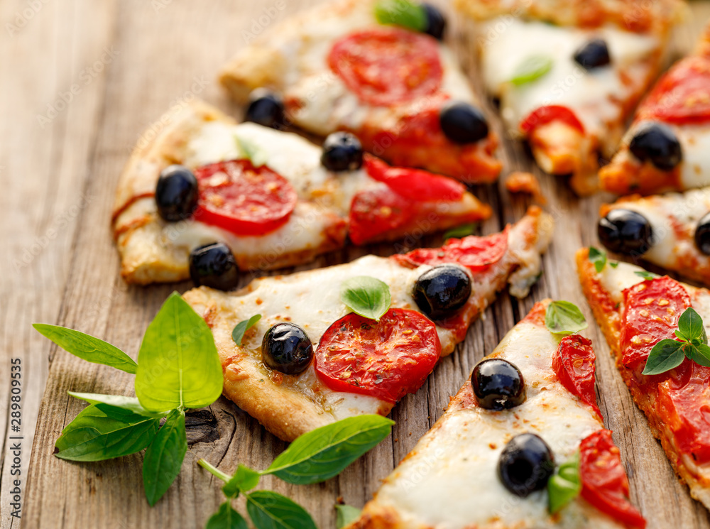 Sliced pizza with tomatoes, black olives, mozzarella cheese and fresh basil on a wooden background, close up. Italian food Sliced pizza with tomatoes, black olives, mozzarella cheese and fresh basil on a wooden background, close up. Italian food