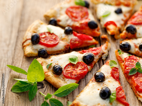 Sliced pizza with tomatoes, black olives, mozzarella cheese and fresh basil on a wooden background, close up. Italian food