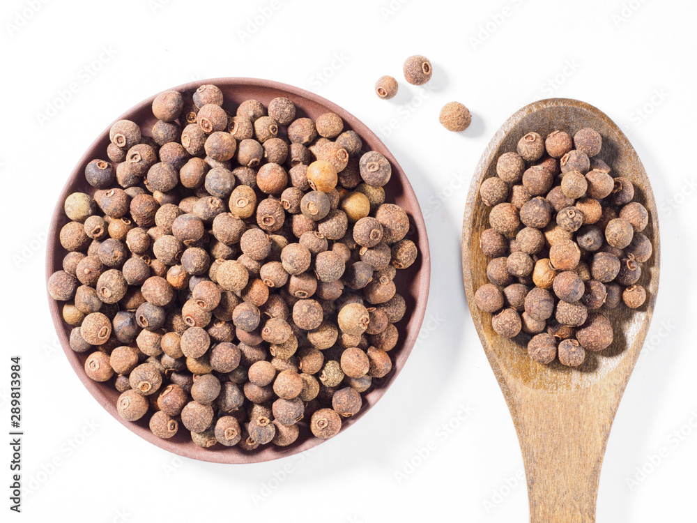 Allspice (Jamaica pepper) in clay plate and wooden spoon vertically on white background Allspice (Jamaica pepper) in clay plate and wooden spoon vertically on white background