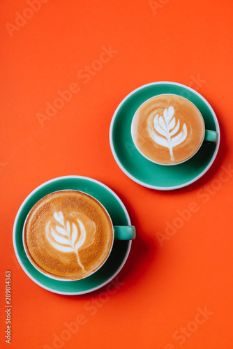 Cyan cappuccino coffee cups over orange background. Top view flat lay with copy space