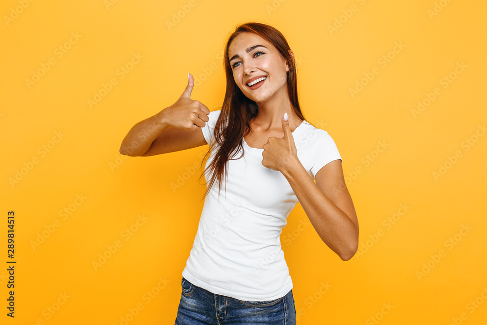 Portrait of a rather attractive woman, showing thumbs up, on a yellow background Portrait of a rather attractive woman, showing thumbs up, on a yellow background
