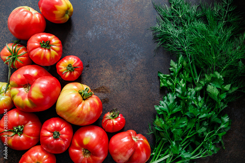 Top view of brandywine sort tomatoes with greens for seasonal canning or salad on a table. photo