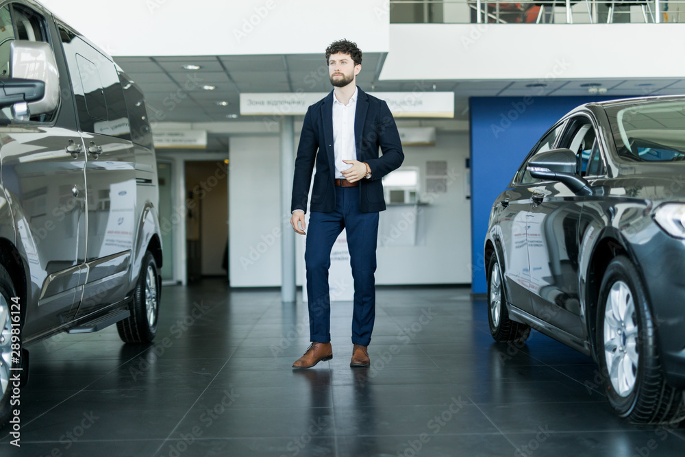 Handsome young man standing near cars in showroom Handsome young man standing near cars in showroom
