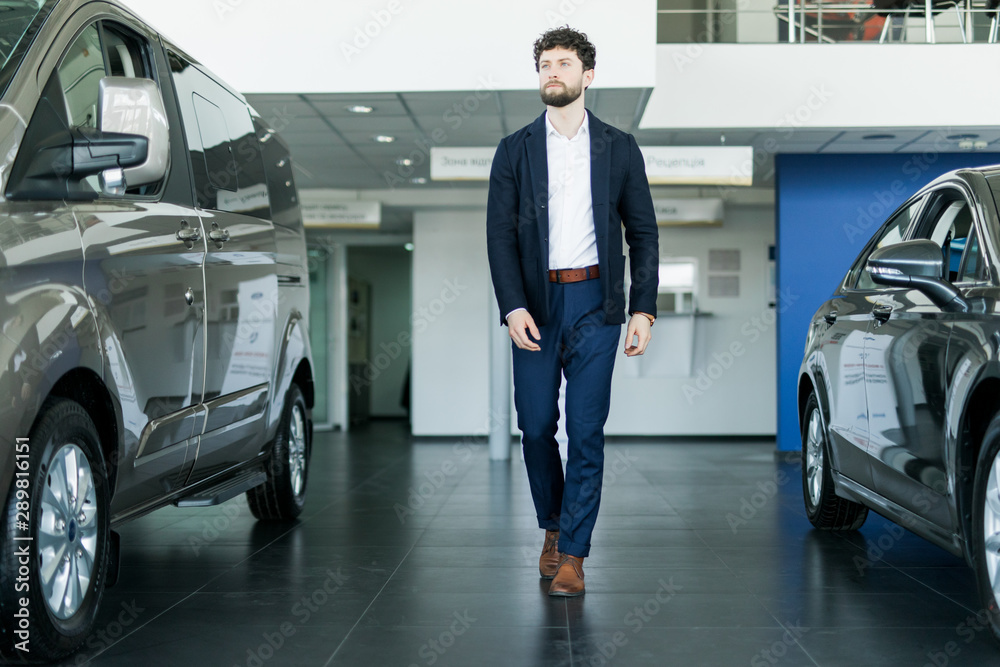 Handsome young man standing near cars in showroom Handsome young man standing near cars in showroom