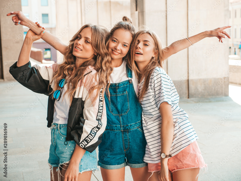 Fototapeta premium Portrait of three young beautiful smiling hipster girls in trendy summer clothes. Sexy carefree women posing on the street background.Positive models having fun.Hugging