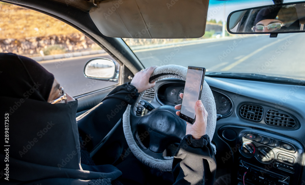 Arabic muslim woman driving a car while using her smart phone