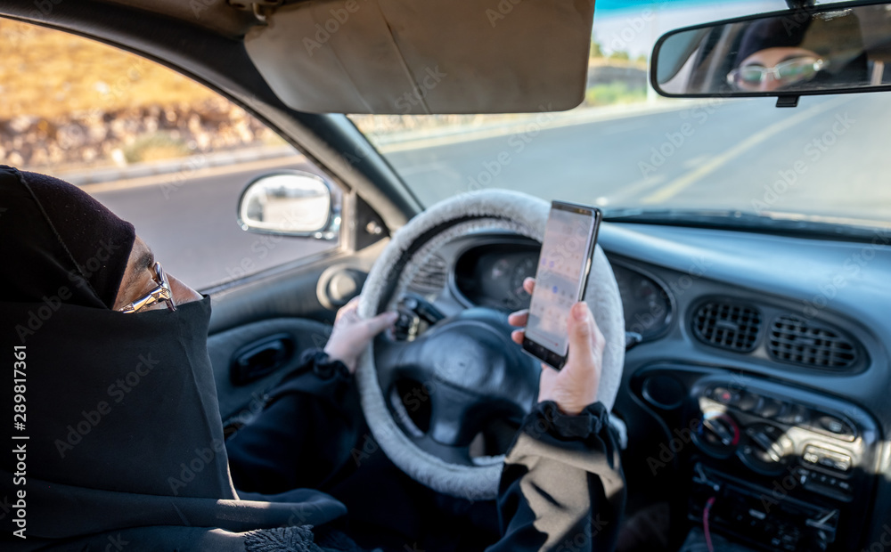 Arabic muslim woman driving a car while using her smart phone