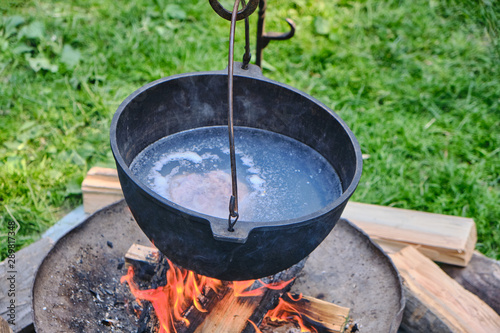 The boiler with a piece of meat in a broth hanging over the fire. Pot of soup on a summer day, lifestyle.