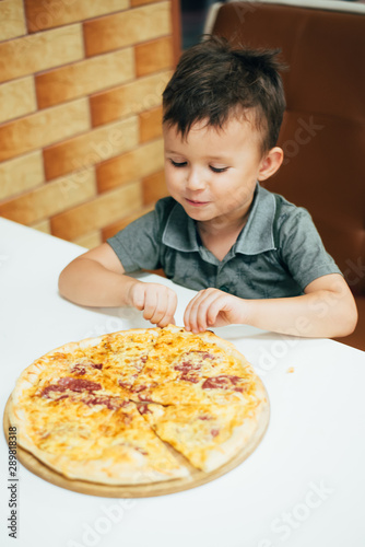 a little boy in a cafe or pizzeria sitting on the couch on the table on the stand a whole pizza, waiting for it to cool down and you can eat