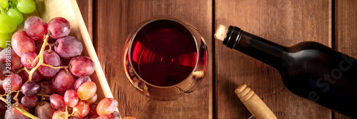 Wine Tasting Panorama. A red wine glass with a bottle, grapes, and a vintage corkscew, shot from the top on a dark rustic wooden background