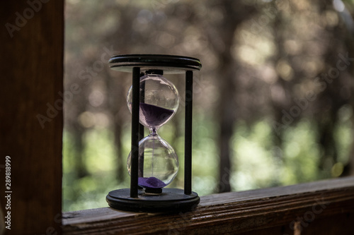 Sand running through the bulbs of an hourglass measuring the passing time in a countdown to a deadline, on a colorful background with copy space. Abstract old sand-glass in forest.