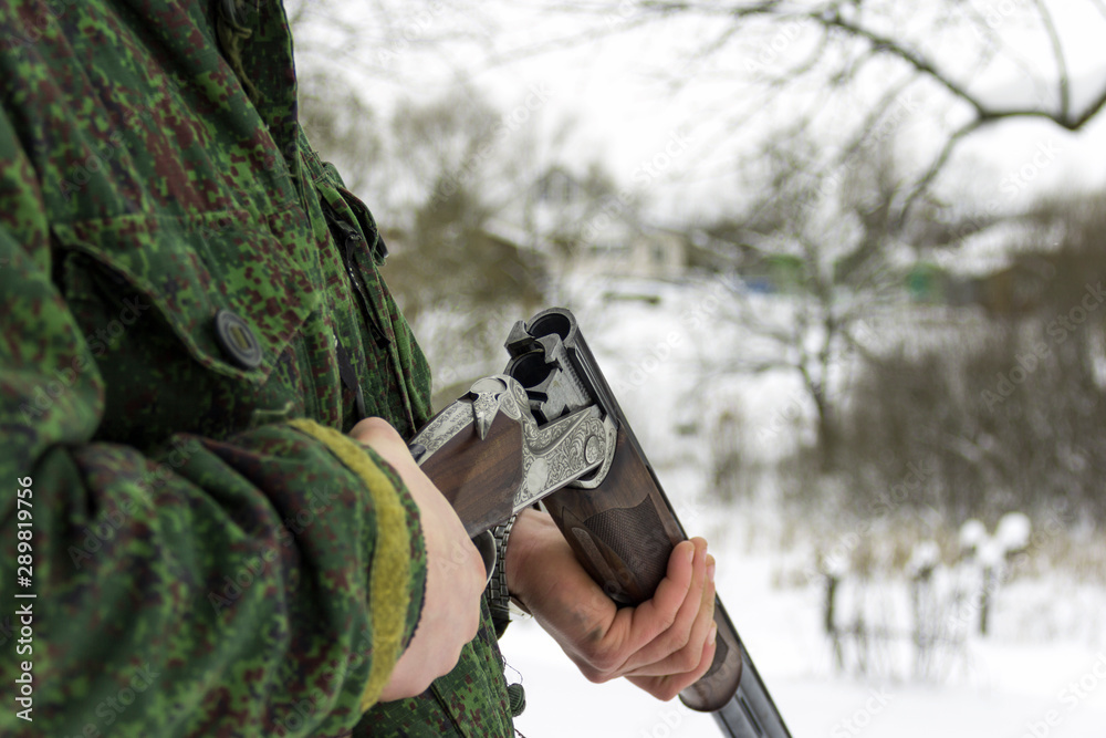 Fototapeta premium Male hunter in camouflage opened hunting rifle. Open double-barreled hunting rifle. Empty trunks without cartridges close-up.