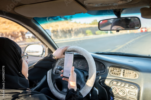 Arabic muslim woman driving a car while using her smart phone