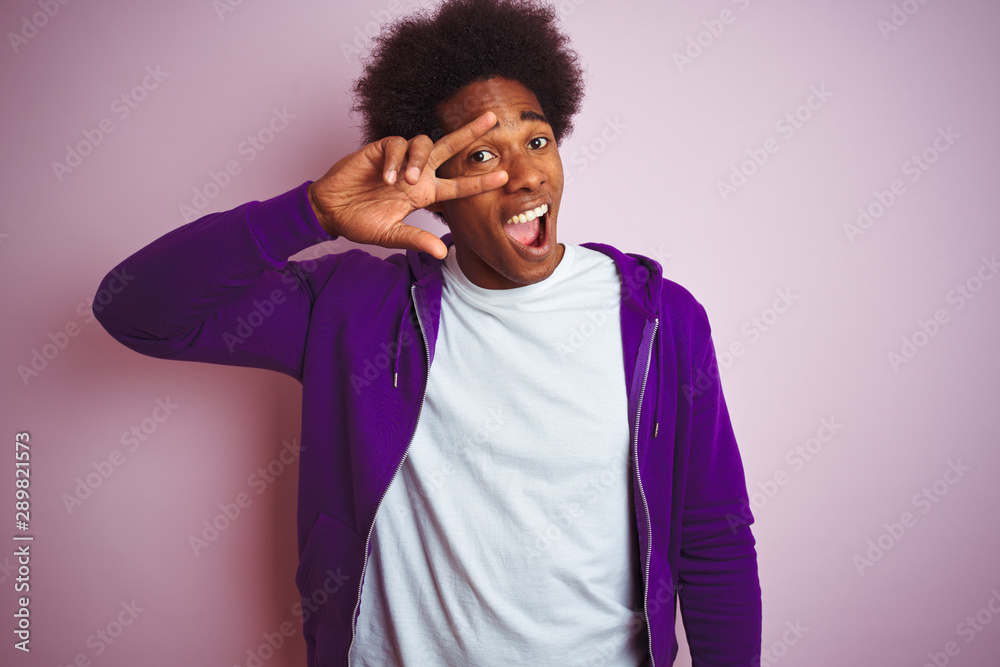 Young african american man wearing purple sweatshirt standing over isolated pink background Doing peace symbol with fingers over face, smiling cheerful showing victory Young african american man wearing purple sweatshirt standing over isolated pink background Doing peace symbol with fingers over face, smiling cheerful showing victory