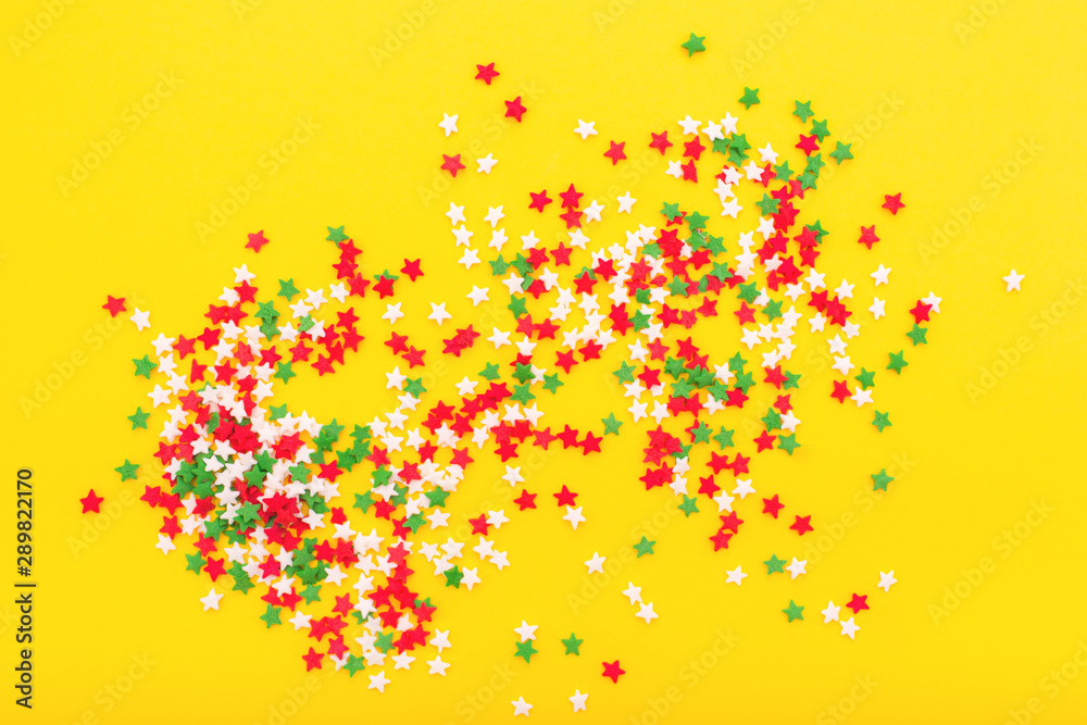 Colorful festive stars sprinkles as a frame on yellow background. Flat lay style. Top view.