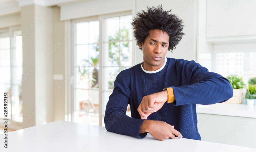 Young african american man wearing casual sweater sitting at home Checking the time on wrist watch, relaxed and confident