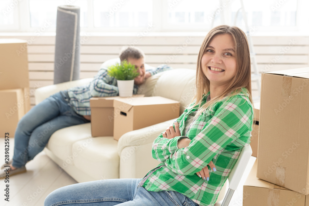 Positive smiling young girl sitting against her laughing blurred husband in a new living room while moving to a new home. The concept of joy from the possibility of finding new housing. Positive smiling young girl sitting against her laughing blurred husband in a new living room while moving to a new home. The concept of joy from the possibility of finding new housing.