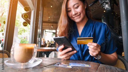 Closeup image of asian woman using credit card for purchasing and shopping online on mobile phone
