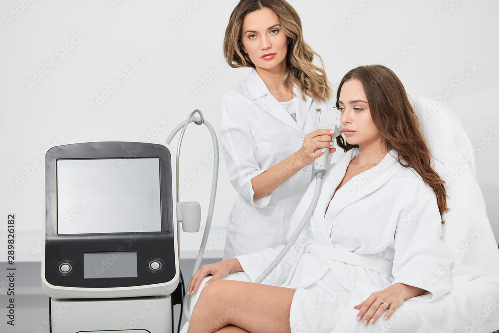 Obraz premium talented beautician doing rf-lifting procedure for young woman sitting in a beauty salon. close up photo. job, profession, occupation