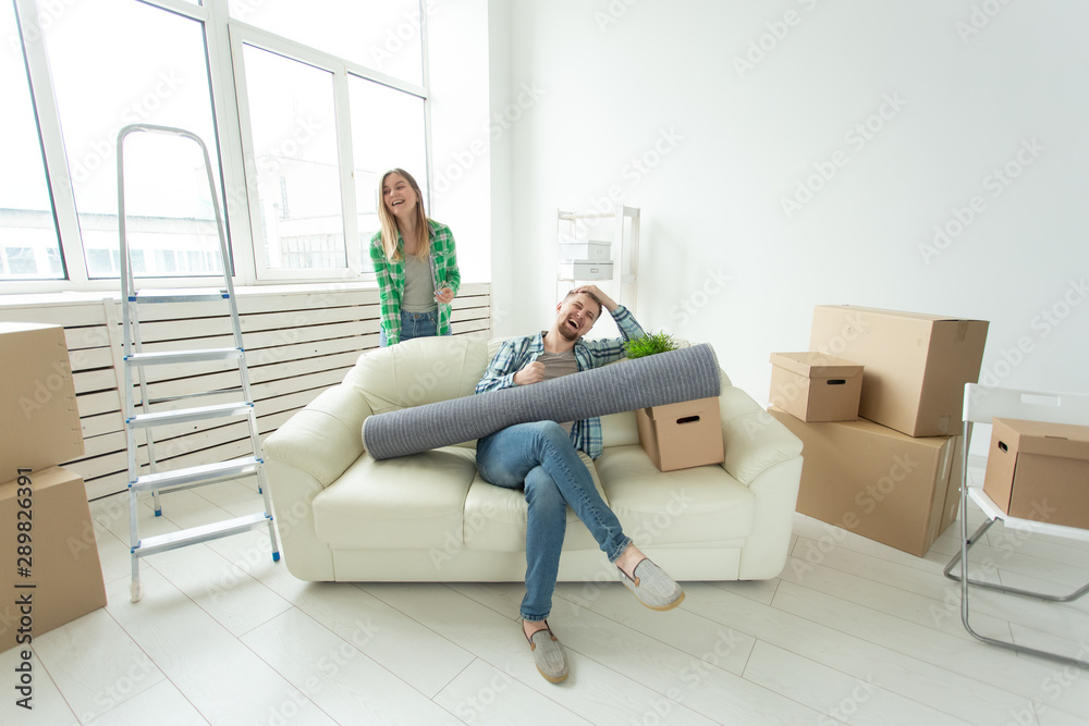 Positive crazy cheerful couple rejoices in moving their new apartment sitting in the living room with their belongings. Concept of housewarming and mortgages for a young family. Positive crazy cheerful couple rejoices in moving their new apartment sitting in the living room with their belongings. Concept of housewarming and mortgages for a young family.
