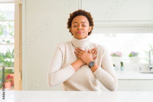 Young beautiful african american woman at home smiling with hands on chest with closed eyes and grateful gesture on face. Health concept.